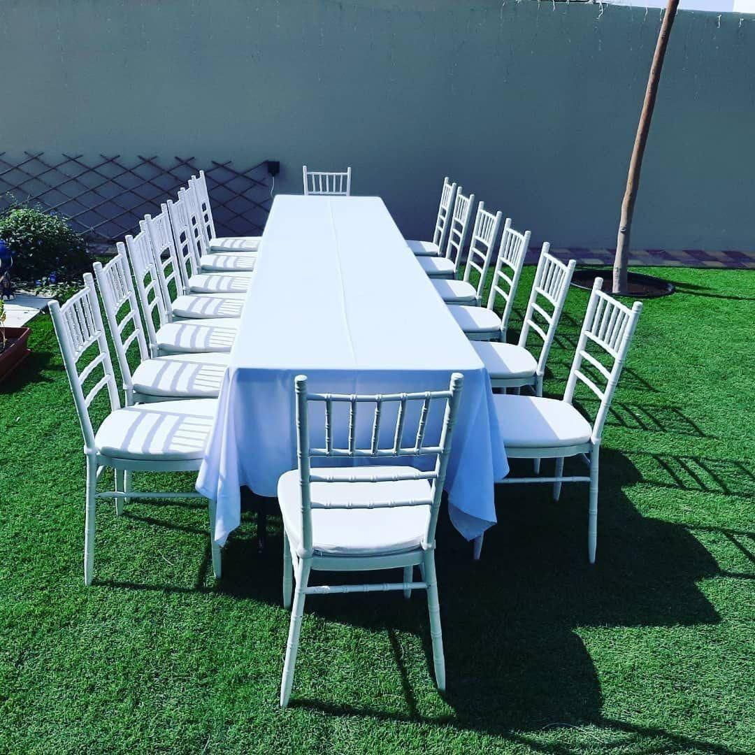 Long banquet table with white chairs for outdoor rental setup